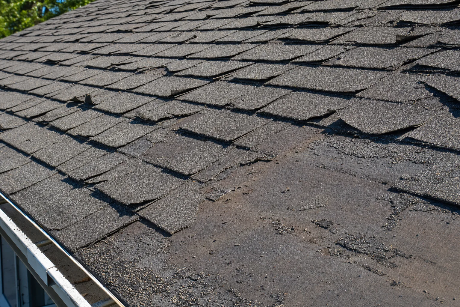 An aged asphalt shingle roof showing widespread granule loss, curling shingle edges and exposed bitumen across the whole surface