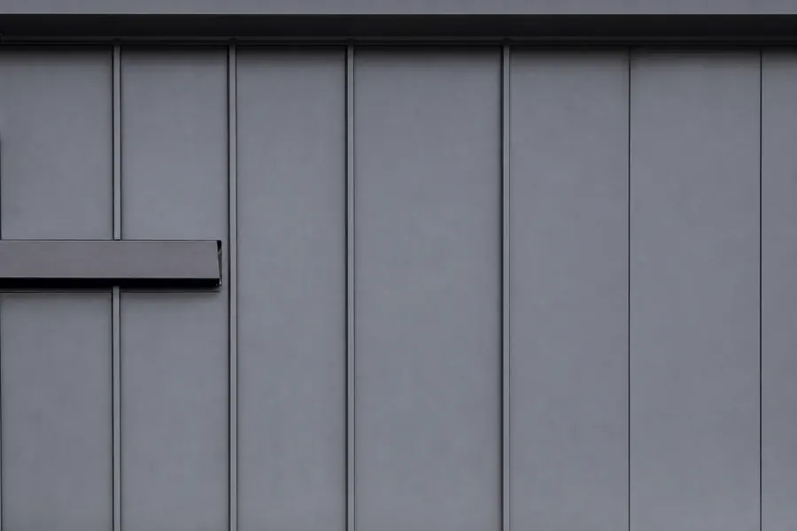 Dark charcoal standing seam steel siding with flat panels separated by raised vertical seams and a matte factory finish.