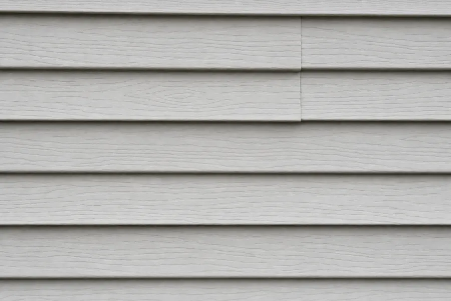 Pale grey vinyl lap siding with a slight satin sheen, crisp shadow lines at each overlap and a visible vertical butt joint where two panels lap.