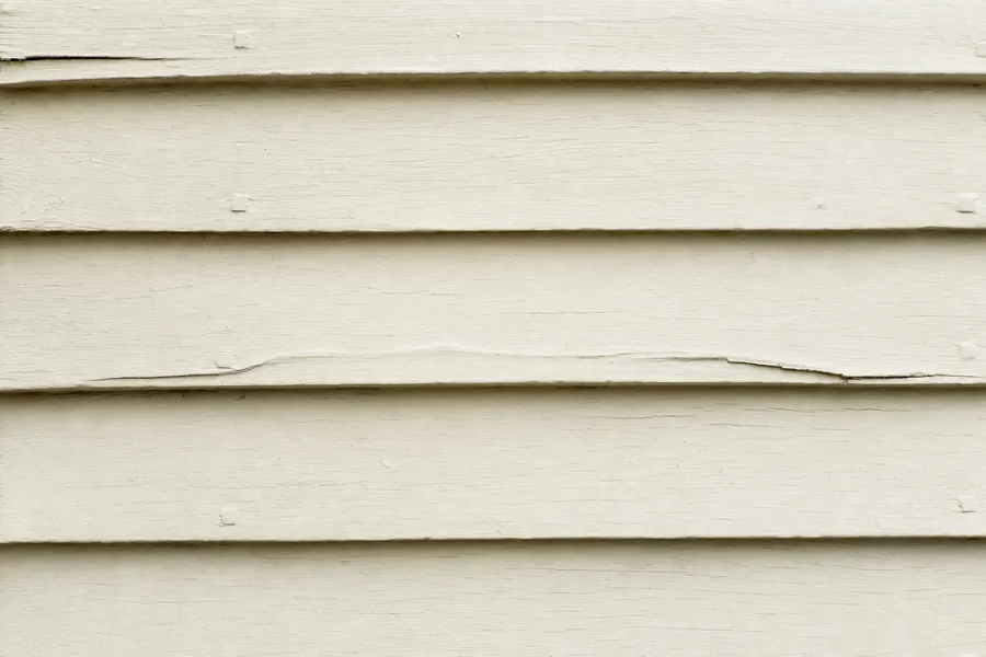 Narrow painted wood clapboard boards overlapping horizontally, with visible brush texture, fine checking in the grain and square nail heads.